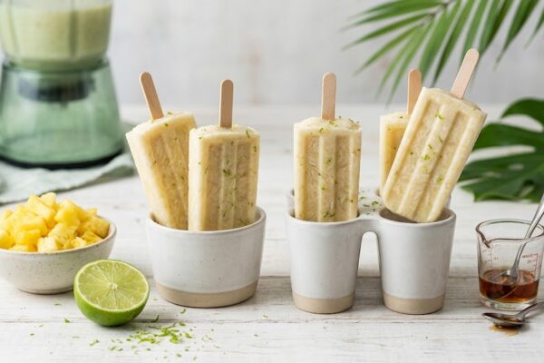 Gelados de Abacaxi e Coco em Sobre SIBO Gelados de abacaxi artesanais com raspas de lima, servidos ao lado de fruta fresca, xarope de ácer e um liquidificador.